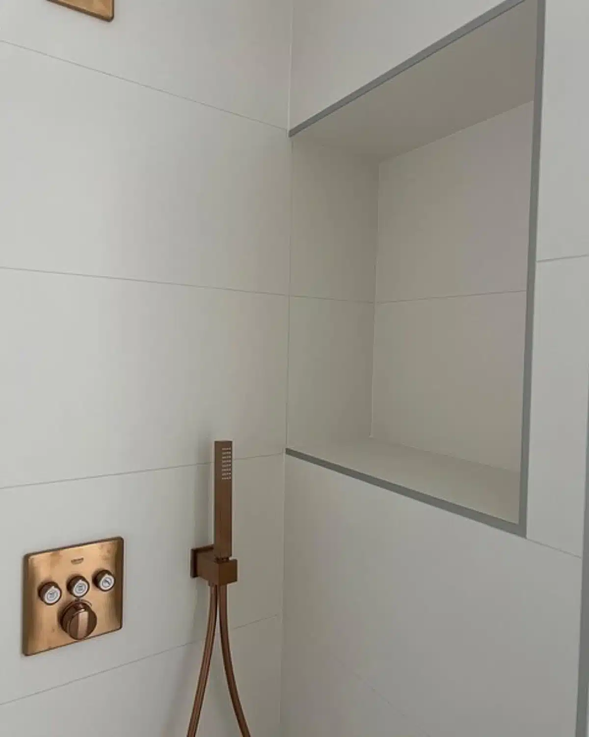 Robinetterie dorée murale avec niche encastrée dans une douche moderne