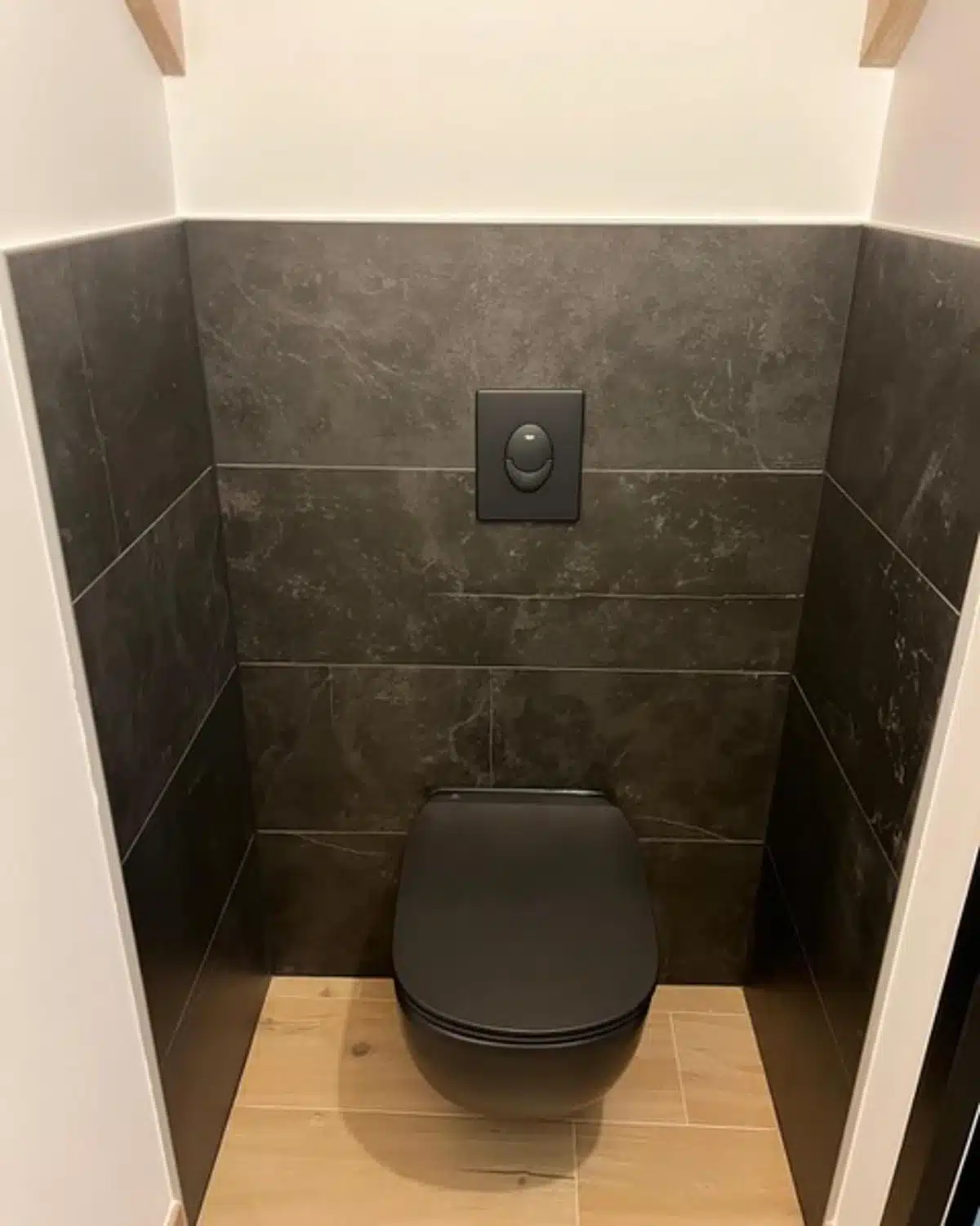 Toilettes suspendues avec carrelage effet pierre foncée et plaque de commande noire