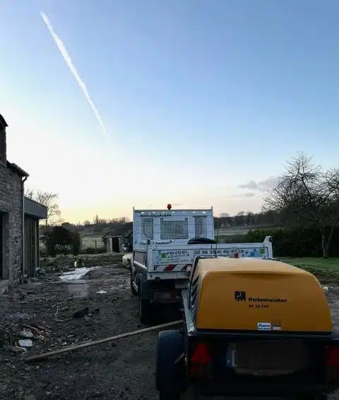 Camion benne FAVREL JOHNNY et remorque avec pompe à béton Putzmeister SP 20 THi sur chantier, sous ciel bleu avec traînée. Tel: 02 96 39 41 41.