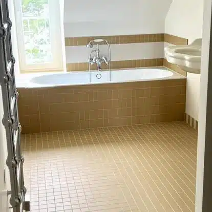 Salle de bain avec baignoire encastrée, robinetterie chromée, carrelage mural et au sol marron clair, et un lavabo en porcelaine.