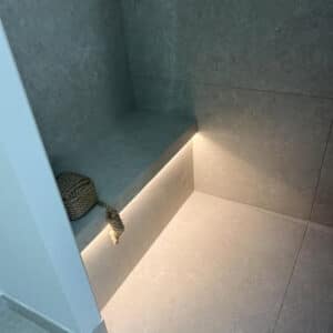 Banquette de douche carrelée avec éclairage LED indirect intégré et dalles effet pierre grise moderne.