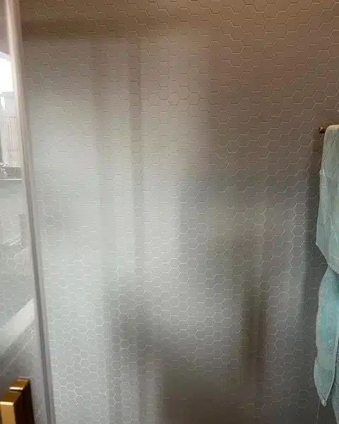 Paroi de douche en carrelage mosaïque hexagone gris clair avec serviette bleue et poignée dorée.