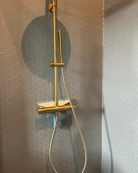 Douche moderne en laiton brossé avec mitigeur et pommeau de douche sur carrelage gris à motifs hexagonaux.