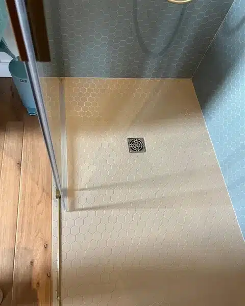 Douche italienne avec carrelage hexagonal bleu et beige, drain central et paroi de verre aux finitions dorées.