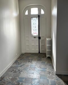 Entrée lumineuse avec carrelage à motifs bleus et porte blanche cintrée.