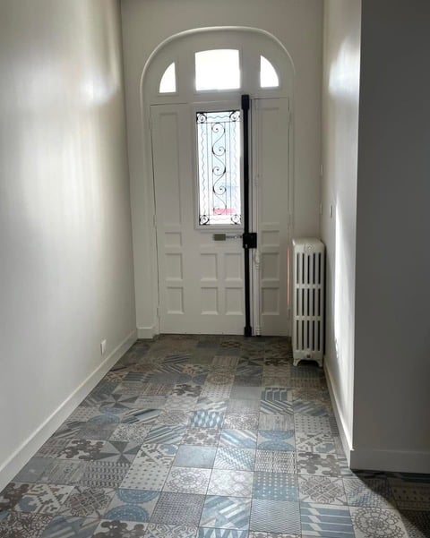 Entrée lumineuse avec carrelage à motifs bleus et porte blanche cintrée.