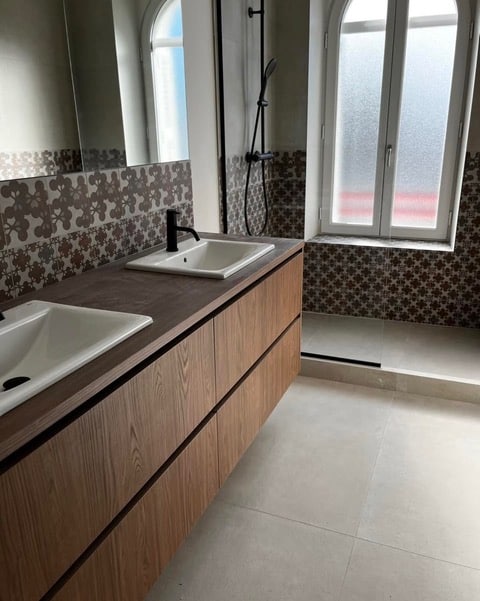 Salle de bain moderne avec double vasque bois, robinet noir et carrelage décoratif.